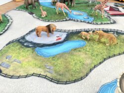 Kinderspielteppich Zoo mit abgebildeter Löwenfamilie aus Spieltieren auf grasgrünem Gehege