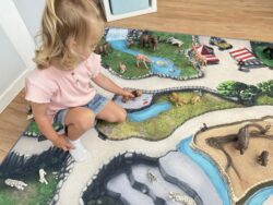 Mädchen spielt mit Löwen auf grünem Zoo-Spielteppich.