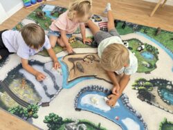 Drei Kinder spielen mit Schleich-Tieren auf Zoo-Spielteppich mit Eis- und Savannengehegen.
