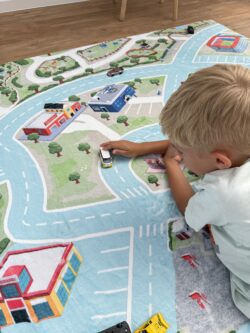 Junge fährt Spielzeugauto über den Fluffy Town Spielteppich – Nahaufnahme