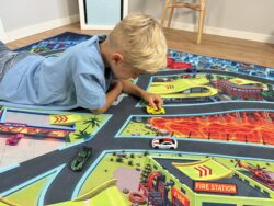 Kind spielt mit gelbem Auto auf Spielteppich „Monster City XL“ 200×140 cm mit Feuerwache und Lavafeld
