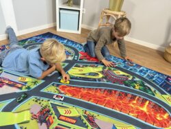Zwei Kinder spielen auf dem Spielteppich „Monster City XL“ 200×140 cm mit Autos, Lavafeld und Rampen