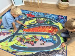 Zwei Kinder spielen mit Autos auf dem Spielteppich „Monster City XL“ 200×140 cm mit Lavafeld und Rampen