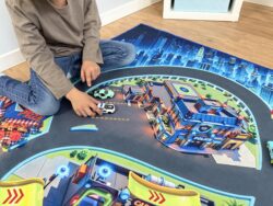 Kind spielt mit Polizeiauto auf Spielteppich „Monster City XL“ 200×140 cm mit Polizeistation und Car Wash
