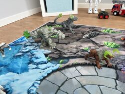 Fantasy-Spielteppich ‘Fantasy World’ mit Stein- und Eiswelt; mehrere Felsen-Kreaturen und Figuren stehen an der Grenze der beiden Welten.